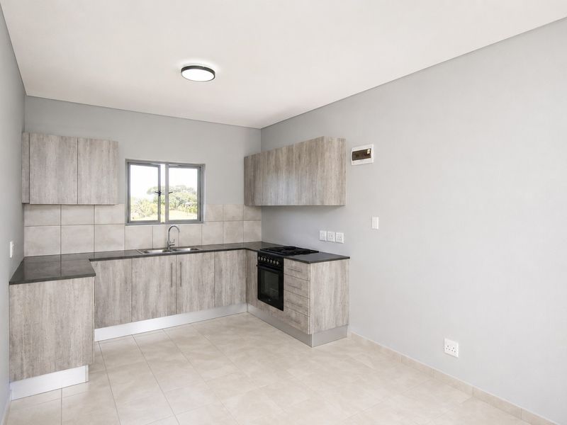A clean, modern kitchen featuring light wood-grain cabinetry, dark countertops, a built-in oven and hob, and neutral tiled flooring.