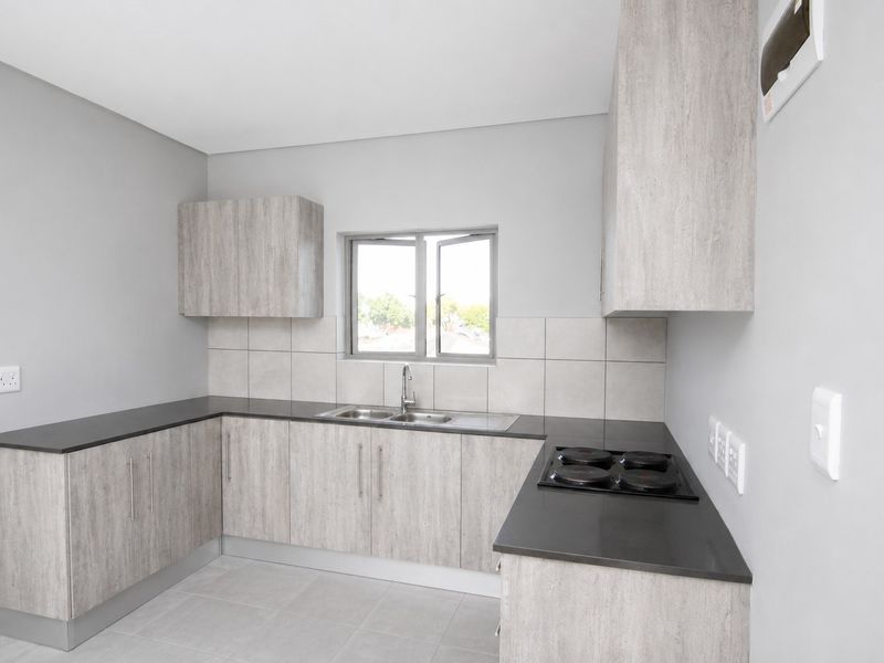 Modern kitchen featuring light wood-grain cabinetry, dark countertops, a built-in electric hob, and neutral tiled finishes in a clean, contemporary layout.