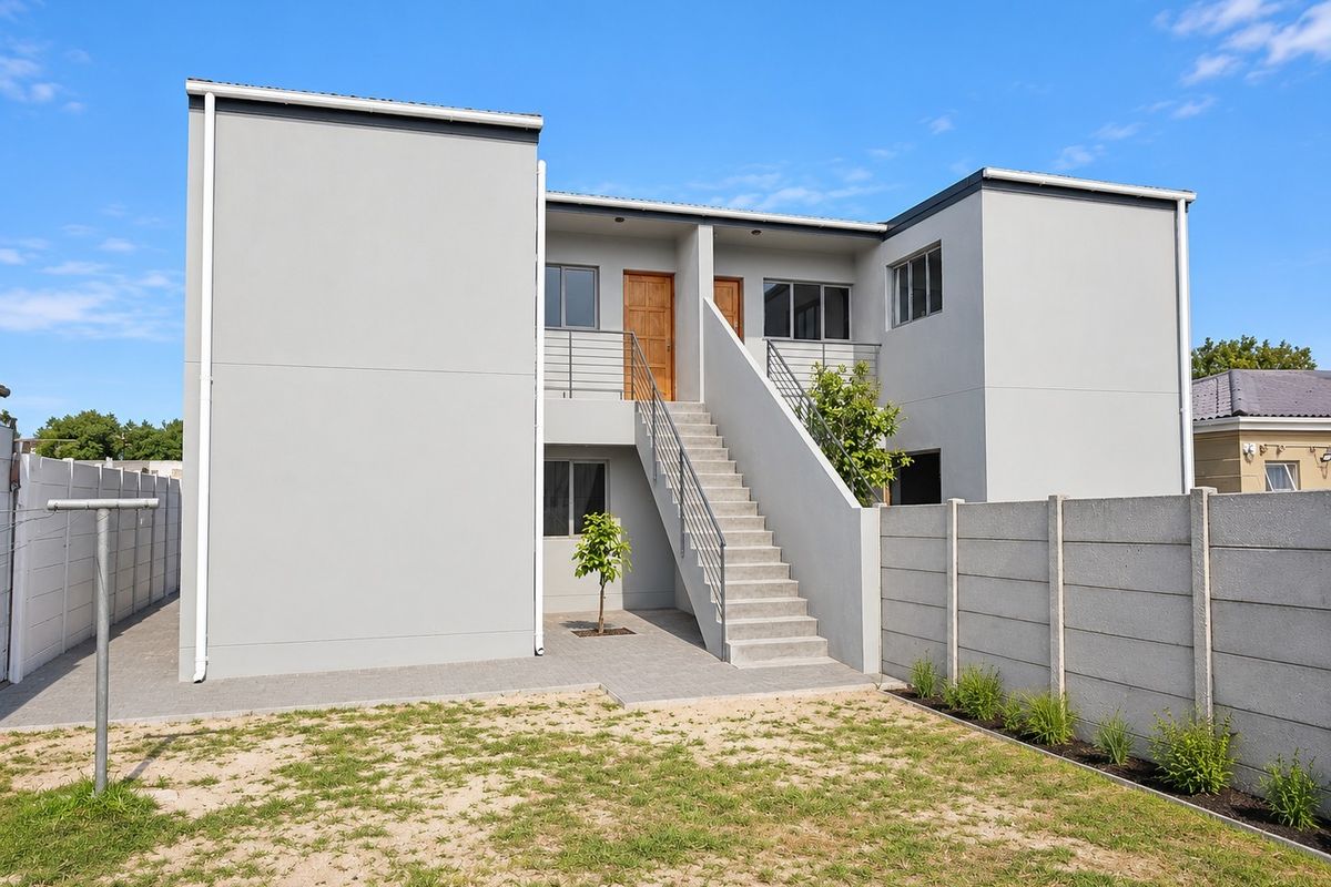 Rear view of a modern two-story residential building featuring a concrete staircase, paved courtyard area, and secure boundary walling.