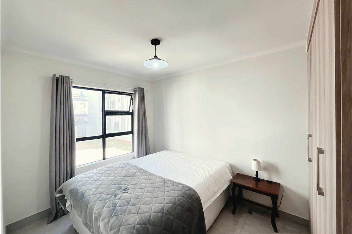 A clean and well-maintained bedroom featuring neutral tiled flooring, a built-in wardrobe, and a large window allowing for natural light.