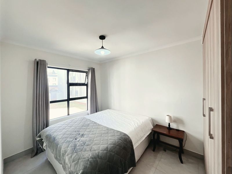A clean and well-maintained bedroom featuring neutral tiled flooring, a built-in wardrobe, and a large window allowing for natural light.