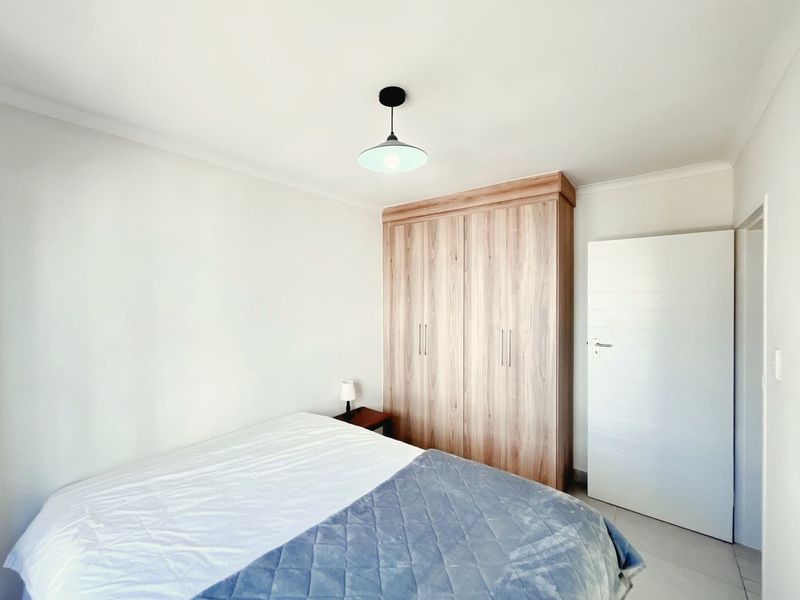 A clean and well-maintained bedroom featuring light wood-finish built-in wardrobes, neutral walls, and tiled flooring.
