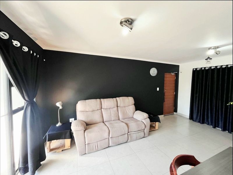 A living room featuring neutral tiled flooring, a bold black accent wall, and modern ceiling lighting, providing a clean and functional living space.