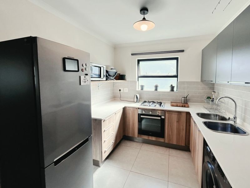 Modern kitchen featuring stone countertops, wood-finish cabinetry, gas hob, built-in oven, and a double sink with tiled backsplash.