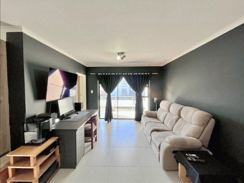 A well-maintained living room featuring neutral tiled flooring, dark accent walls, and a sliding glass door providing access to an outdoor area.
