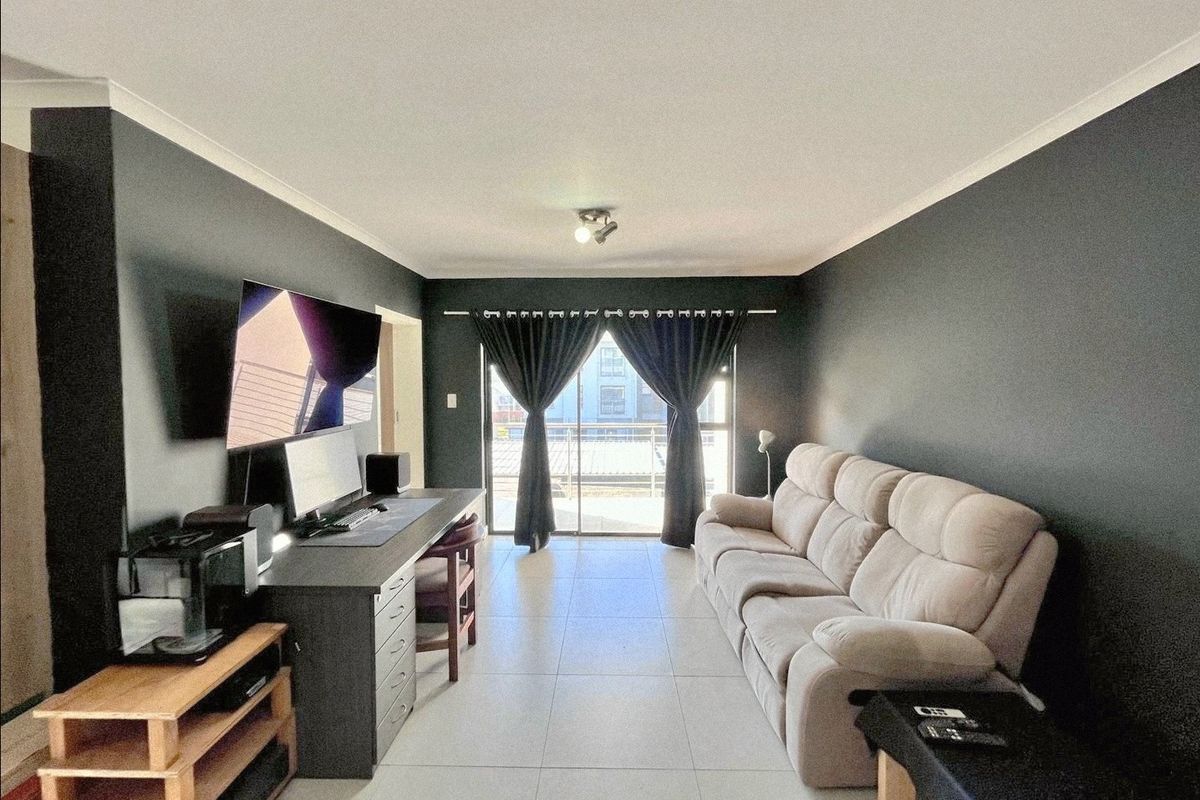 A well-maintained living room featuring neutral tiled flooring, dark accent walls, and a sliding glass door providing access to an outdoor area.