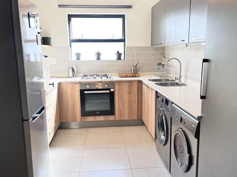 Modern kitchen featuring wood-finish cabinetry, stone countertops, integrated gas hob, electric oven, and dedicated space for laundry appliances with a tiled backsplash.