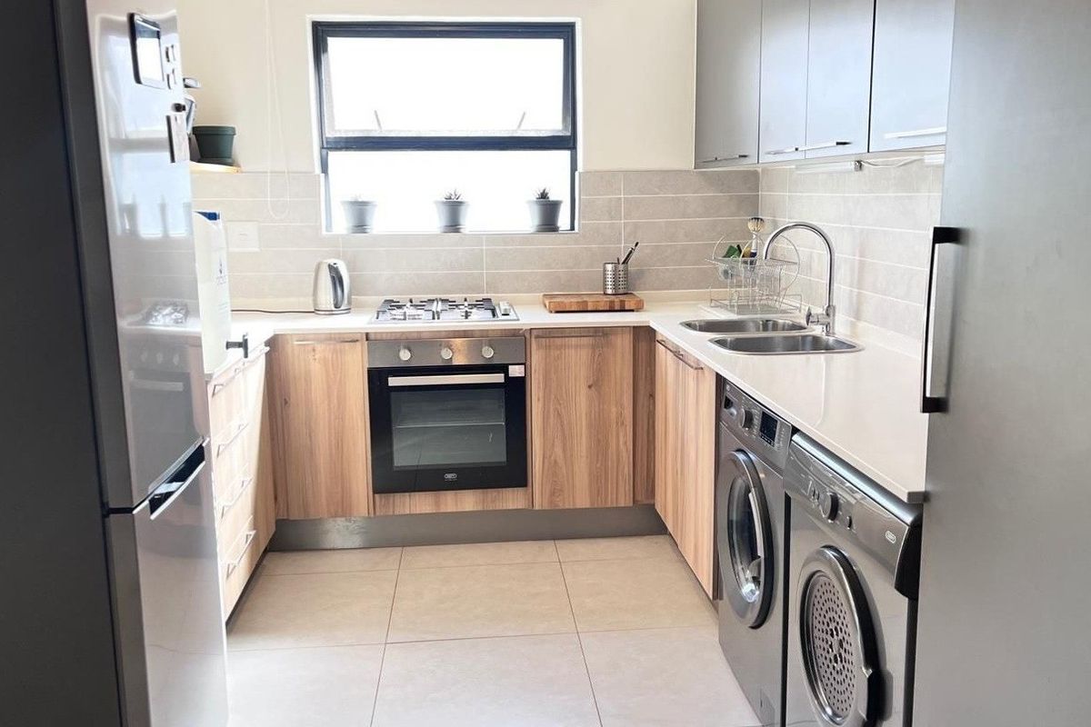 Modern kitchen featuring wood-finish cabinetry, stone countertops, integrated gas hob, electric oven, and dedicated space for laundry appliances with a tiled backsplash.