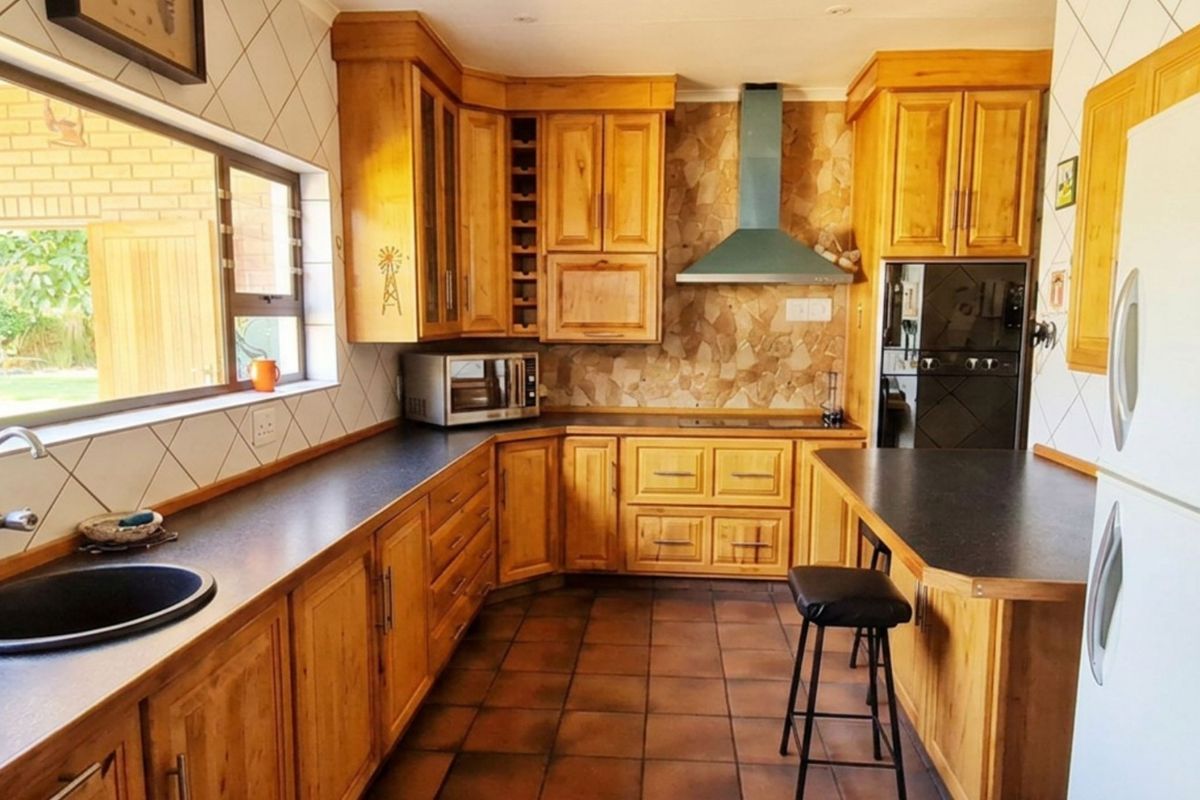 A functional kitchen featuring warm wooden cabinetry, dark laminate countertops, a built-in oven, and a stainless steel extractor fan with tiled backsplash.