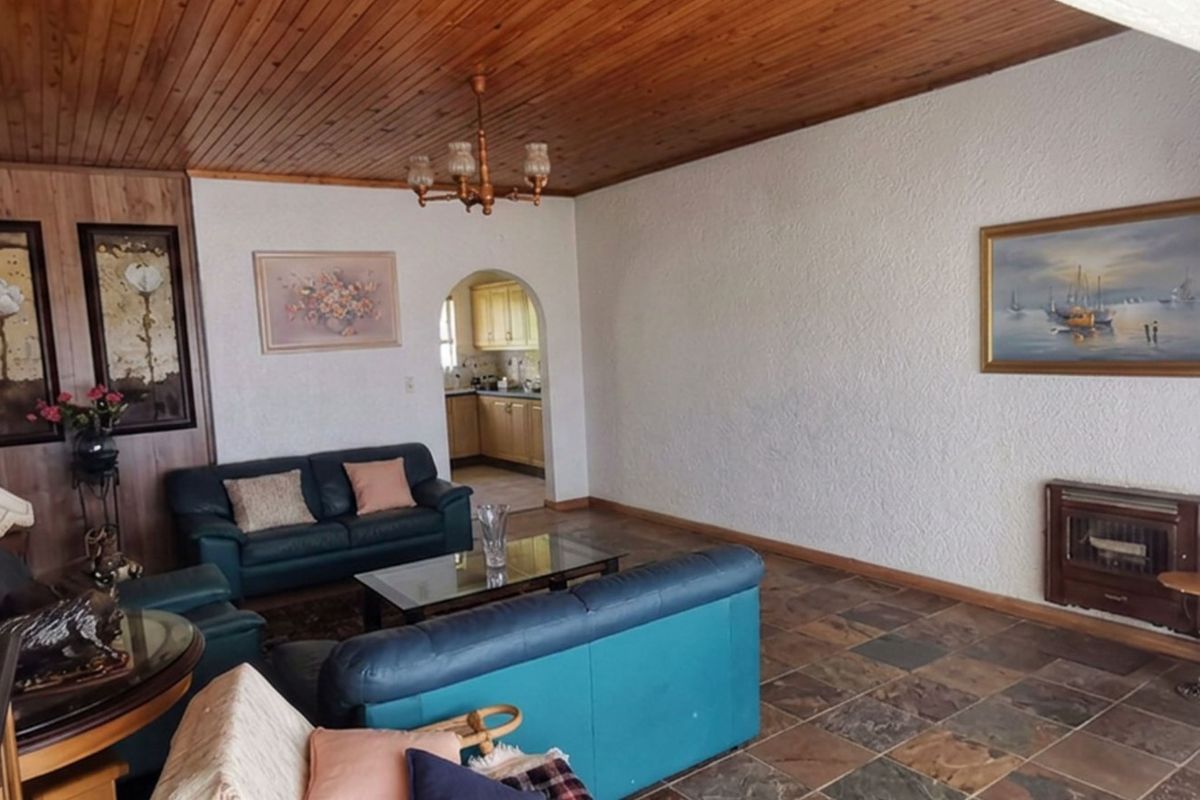 Spacious living room featuring a timber-clad ceiling, stone-tiled flooring, and a built-in fireplace, with an arched entryway leading to the kitchen area.