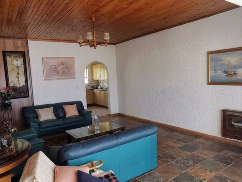 Spacious living room featuring a timber-clad ceiling, stone-tiled flooring, and a built-in fireplace, with an arched entryway leading to the kitchen area.