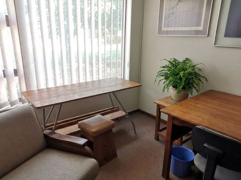 A functional office space featuring carpet flooring and vertical blinds, providing a quiet area suitable for work or study.