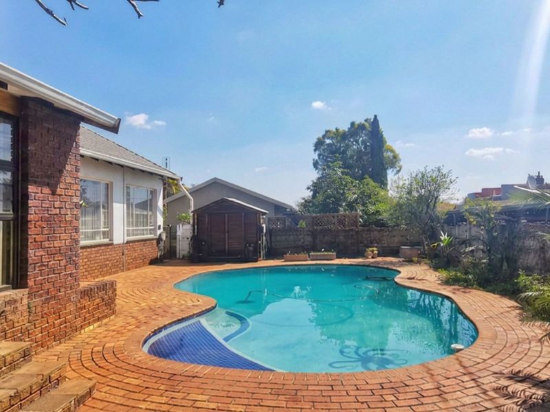 Outdoor pool area featuring a swimming pool with brick paving surround, adjacent to the main house with sliding door access and a garden shed.