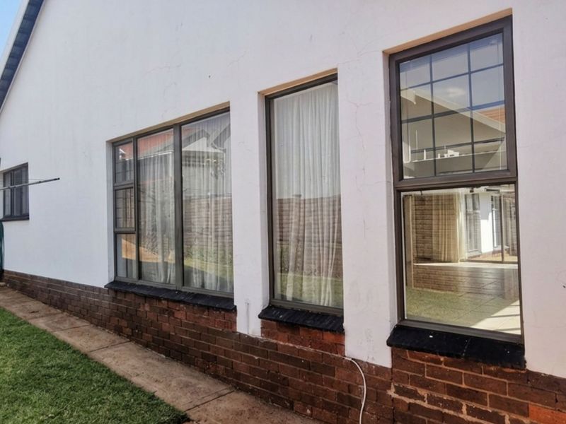 Rear exterior view of the house featuring a brick base, white plastered walls, and aluminium-framed windows overlooking the garden area.