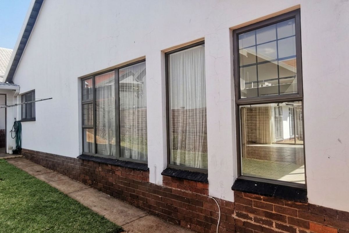 Rear exterior view of the house featuring a brick base, white plastered walls, and aluminium-framed windows overlooking the garden area.