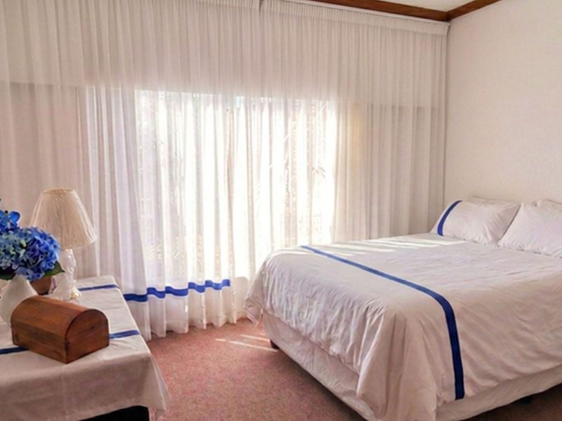 A bedroom featuring carpeted flooring, built-in cupboards, and large windows with floor-to-ceiling curtains allowing natural light.