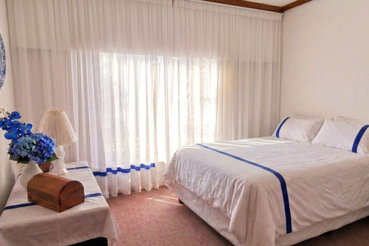 A bedroom featuring carpeted flooring, built-in cupboards, and large windows with floor-to-ceiling curtains allowing natural light.