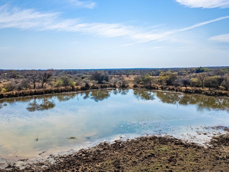 An aerial view of a natural water dam situated within a vast, undeveloped residential land plot featuring native bushveld vegetation.