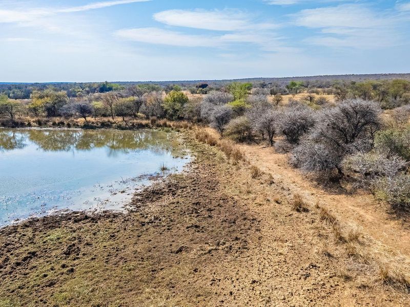 Aerial view of a vacant residential plot featuring a natural dam and established indigenous vegetation, offering a serene landscape setting.