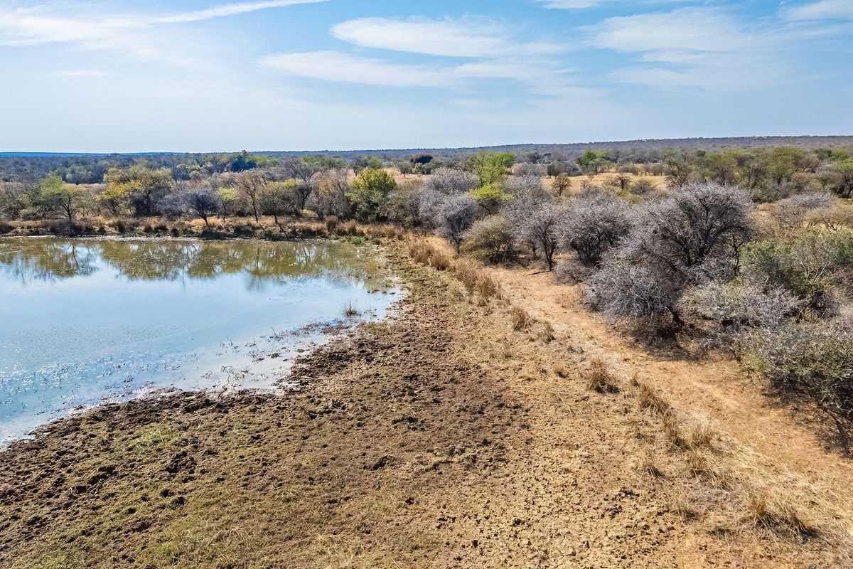 Aerial view of a vacant residential plot featuring a natural dam and established indigenous vegetation, offering a serene landscape setting.