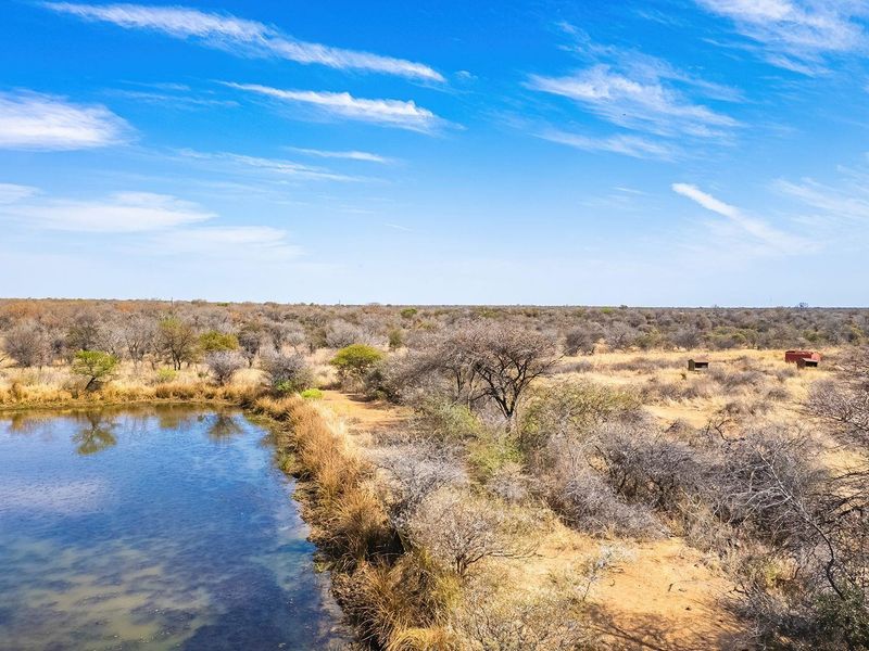 An aerial view of a vacant residential plot featuring a natural pond and native bushveld vegetation under a clear blue sky.