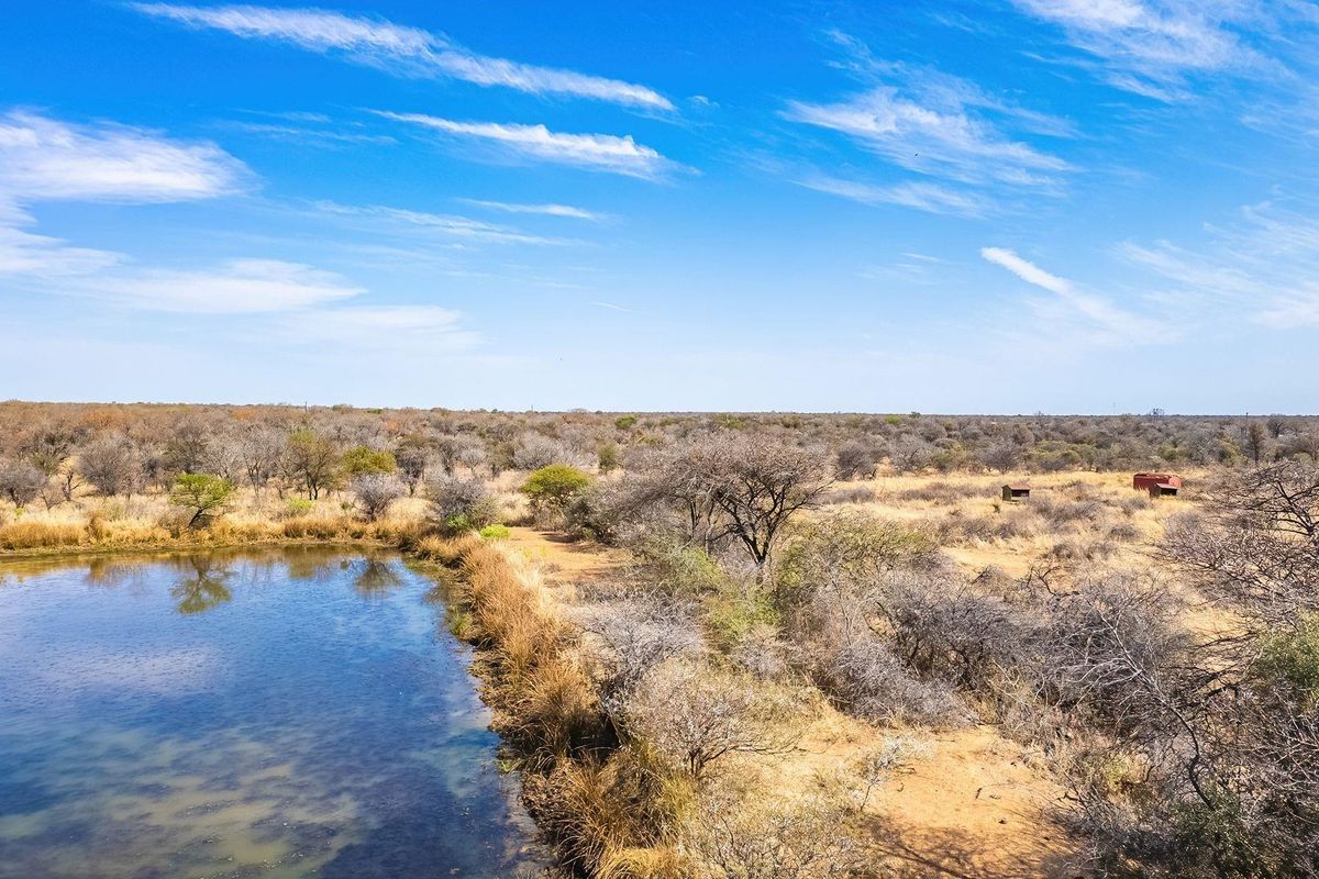 An aerial view of a vacant residential plot featuring a natural pond and native bushveld vegetation under a clear blue sky.