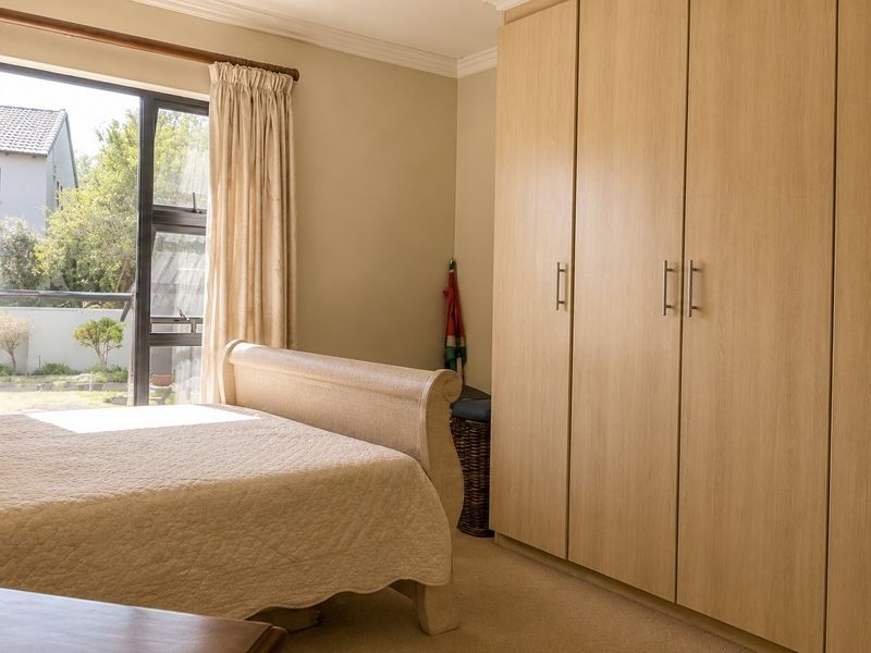 A well-lit bedroom featuring neutral walls, carpeted flooring, and extensive built-in wooden cupboards, with direct access to an outdoor area through a sliding door.