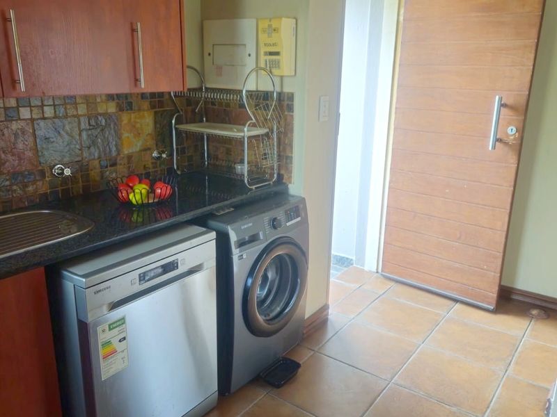 Compact kitchen area featuring wooden cabinetry, granite countertops, stone tile backsplash, and tiled flooring with direct access to an exterior door.