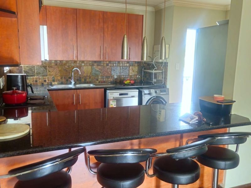 A functional kitchen featuring granite countertops, stone tile backsplash, built-in cabinetry, and integrated appliances with a breakfast bar area.