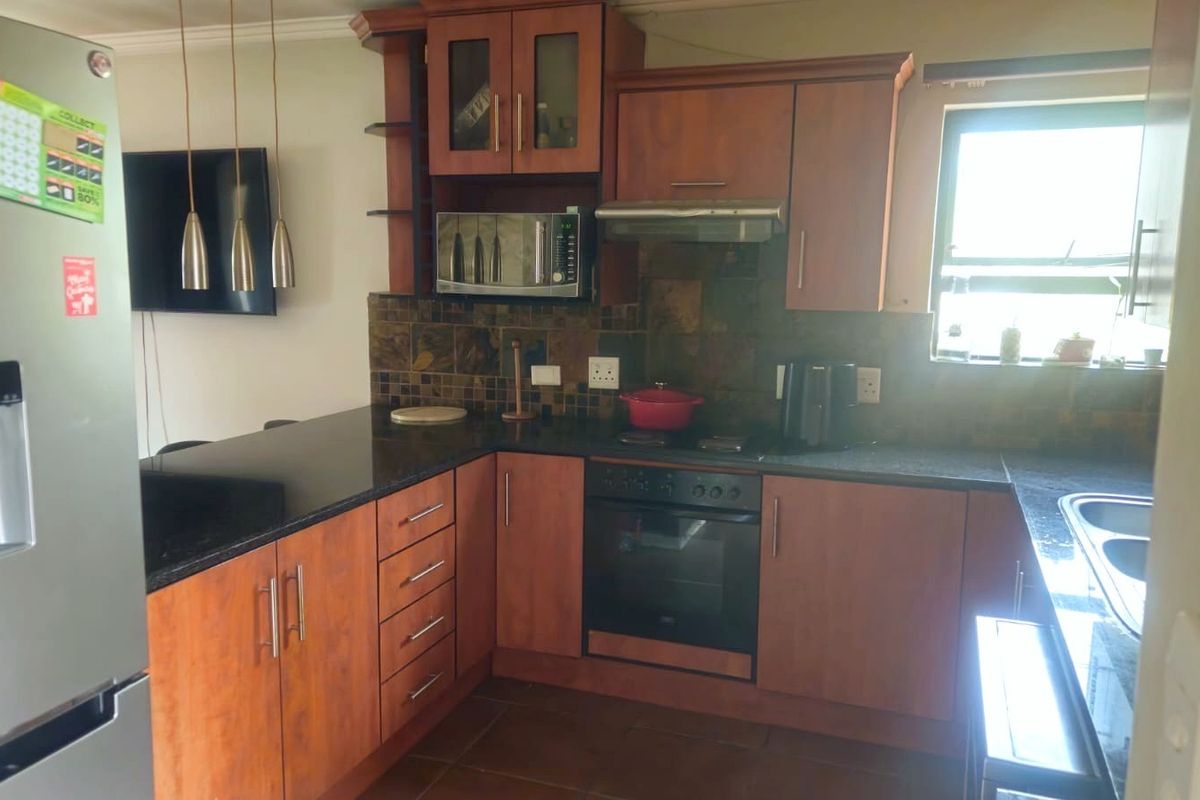 A functional kitchen featuring wood-finish cabinetry, dark granite countertops, a tiled backsplash, and integrated appliances including an oven, hob, and extractor fan.