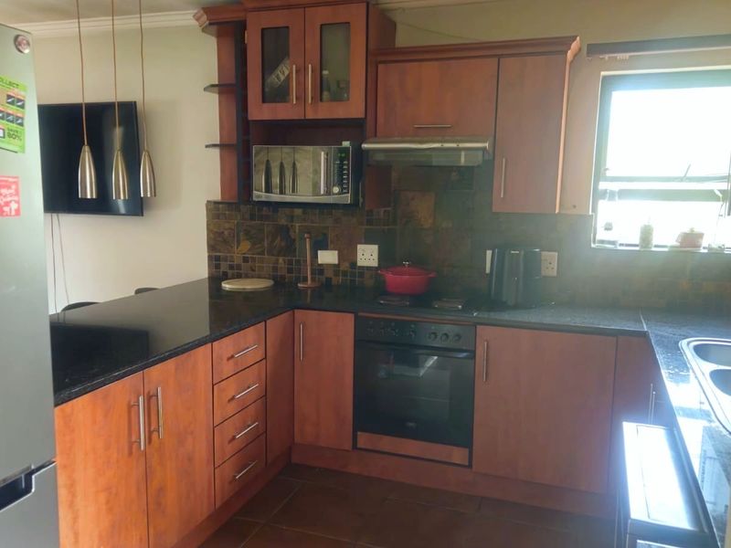 A functional kitchen featuring wood-finish cabinetry, dark granite countertops, a tiled backsplash, and integrated appliances including an oven, hob, and extractor fan.