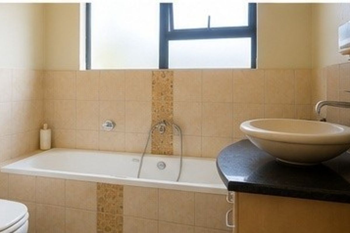 A functional bathroom featuring a built-in bathtub, a vessel sink set on a vanity countertop, and neutral wall tiling.