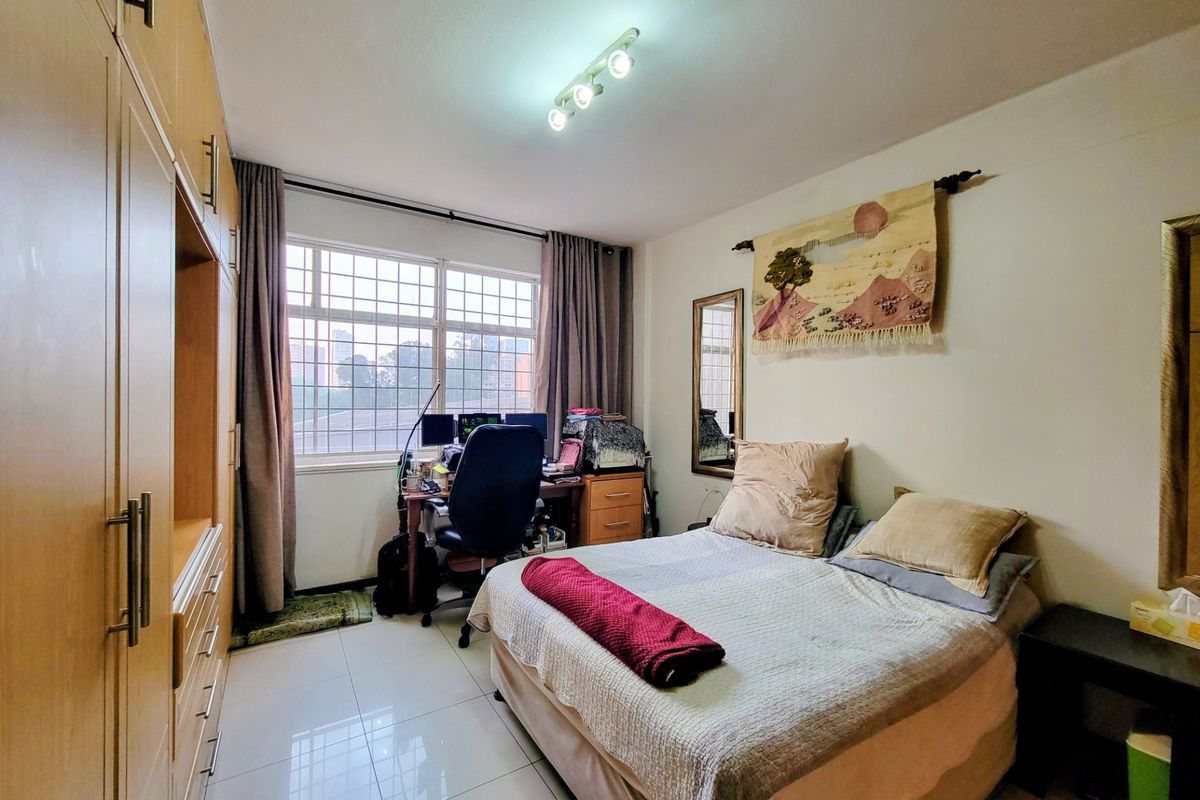 A functional bedroom featuring tiled flooring, a large built-in wardrobe, and a window with security bars, providing natural light and storage space.