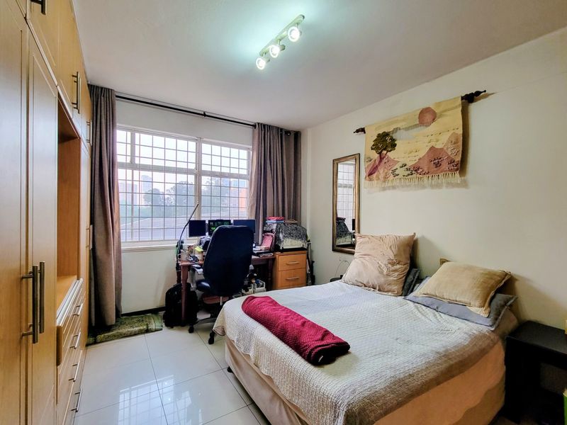 A functional bedroom featuring tiled flooring, a large built-in wardrobe, and a window with security bars, providing natural light and storage space.
