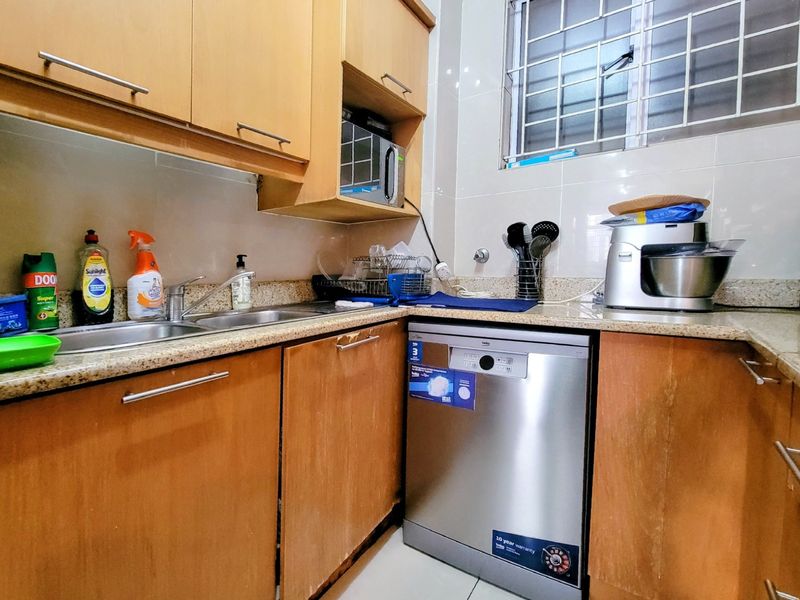 Compact kitchen featuring laminate cabinetry, granite countertops, stainless steel sink, and built-in microwave with a tiled backsplash and security window grille.