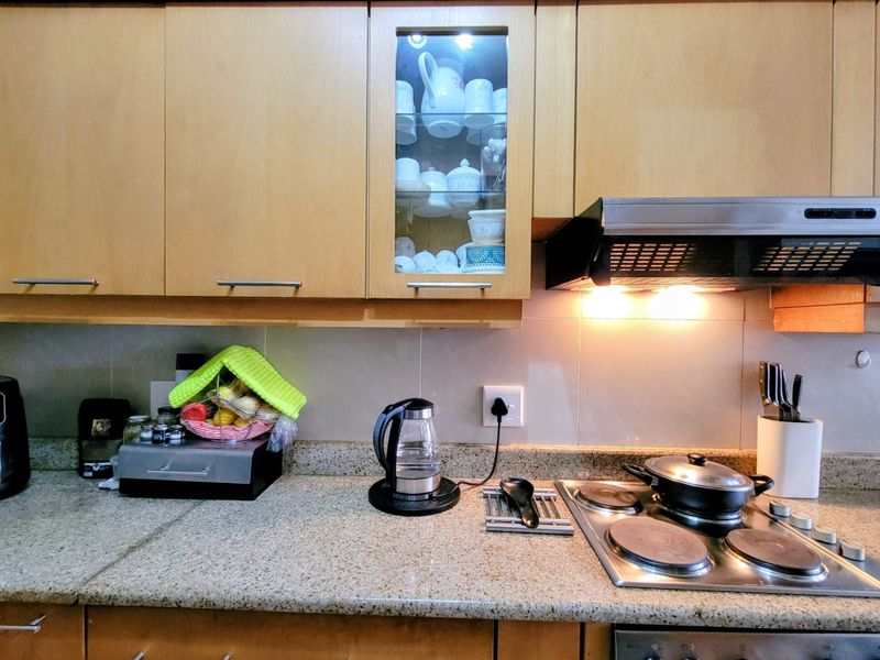 A functional kitchen featuring light wood cabinetry, granite countertops, a tiled backsplash, and a built-in electric hob with an integrated extractor fan.