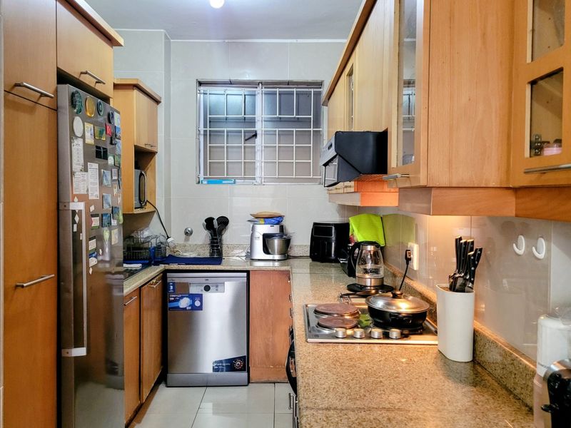 A functional galley-style kitchen featuring wood-finish cabinetry, granite countertops, integrated appliances, and tiled flooring with a window providing natural light.