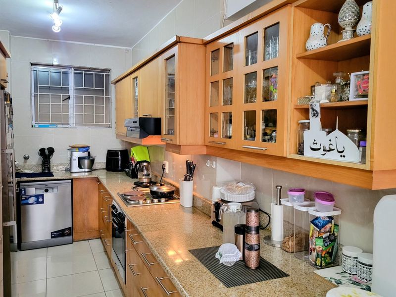 A functional kitchen featuring wooden cabinetry, granite countertops, integrated appliances, and tiled finishes, offering a practical layout with ample storage space.