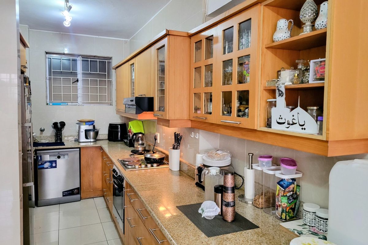 A functional kitchen featuring wooden cabinetry, granite countertops, integrated appliances, and tiled finishes, offering a practical layout with ample storage space.