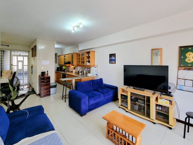 Open-plan living area featuring tiled flooring and a functional kitchen with built-in cabinetry, breakfast bar, and integrated appliances.