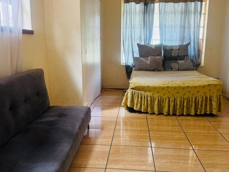 A bedroom featuring tiled flooring, built-in cupboards, and security burglar bars on the windows.