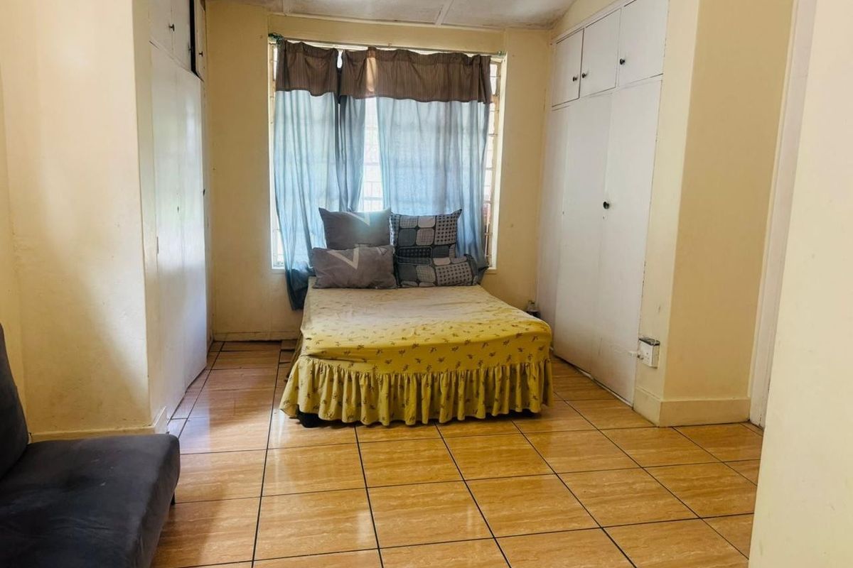 A bedroom featuring tiled flooring, built-in cupboards, and security bars on the window. The room requires cosmetic updates to improve its overall condition.