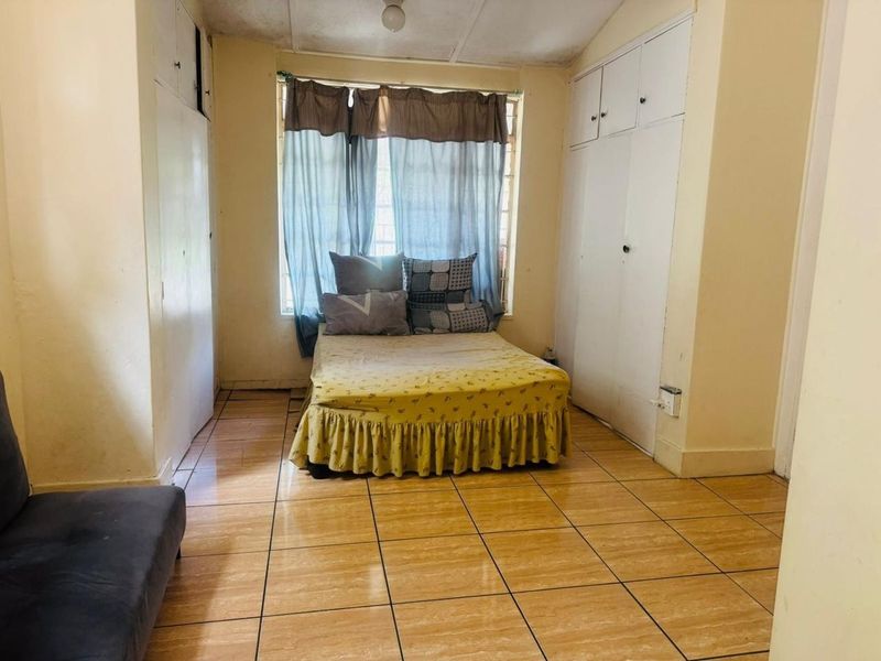 A bedroom featuring tiled flooring, built-in cupboards, and security bars on the window. The room requires cosmetic updates to improve its overall condition.