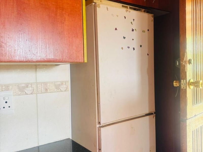 A compact kitchen area featuring dark granite countertops, tiled backsplash, and wooden cabinetry with visible signs of wear.