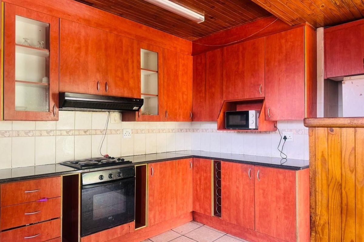 A functional kitchen featuring warm-toned timber cabinetry, granite countertops, built-in oven, hob, extractor fan, and a distinctive timber-clad ceiling.