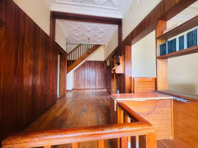 Spacious hallway featuring classic timber wall paneling, original timber flooring, and an ornate pressed metal ceiling with a staircase leading to the upper level.