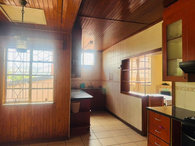 A functional kitchen featuring wooden ceiling and wall paneling, tiled floors, built-in cabinetry, and a stone countertop with a view into the adjacent living area.