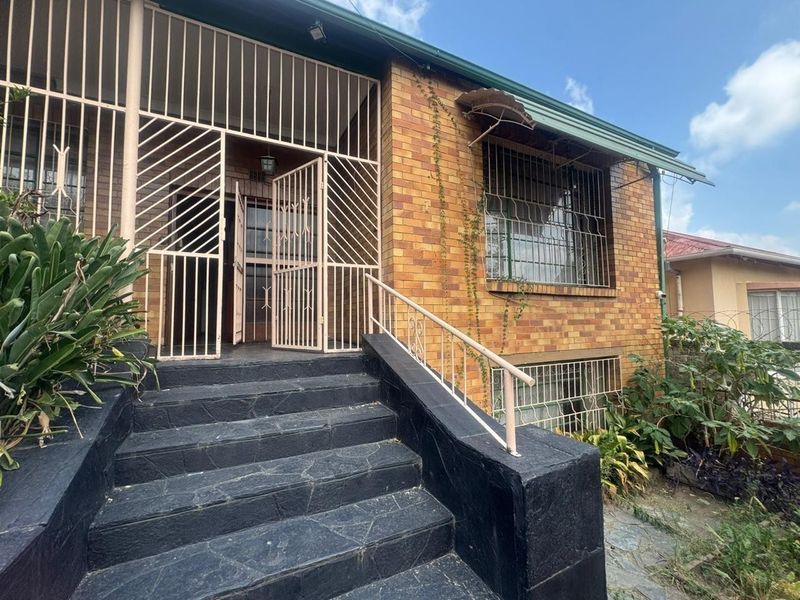 Front entrance of a brick house featuring stone stairs, security gates, and protective window bars, showing signs of age and weathering.