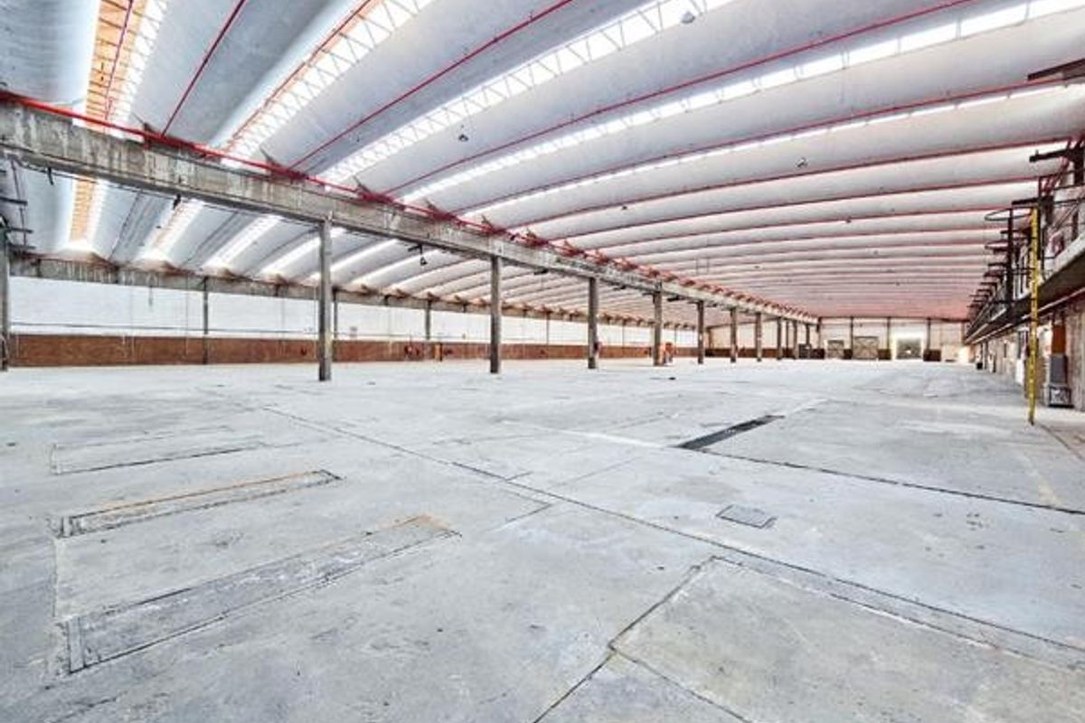 Expansive industrial warehouse space featuring high ceilings with skylights, concrete flooring, and robust steel structural columns, suitable for manufacturing or logistics operations.