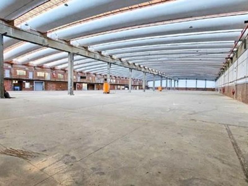 Expansive industrial warehouse space featuring high ceilings with exposed ducting, concrete flooring, and robust steel structural columns.